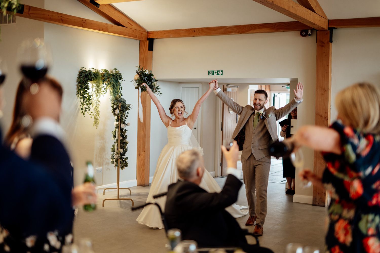 Wedding reception venue with exposed wooden beams and guests mingling in the background.
