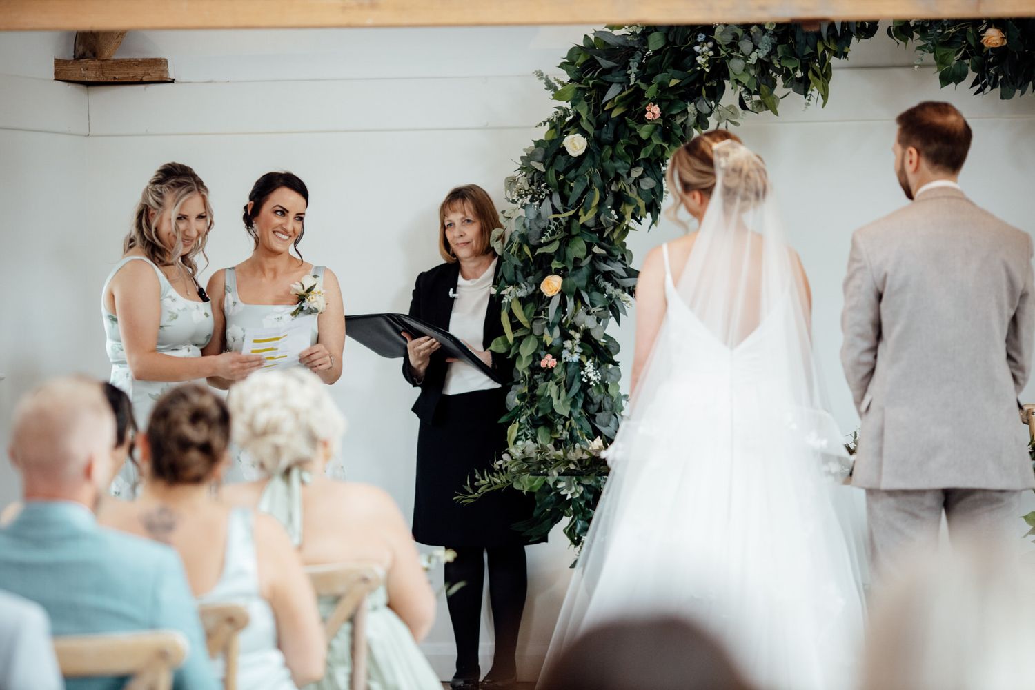 Indoor wedding ceremony with guests seated in rows and greenery decorations.