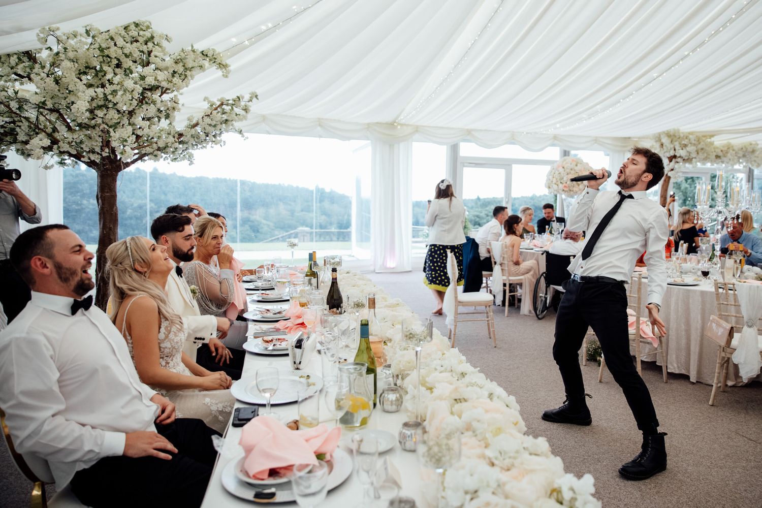 Elegant white wedding reception tent with floral centerpieces and table settings.