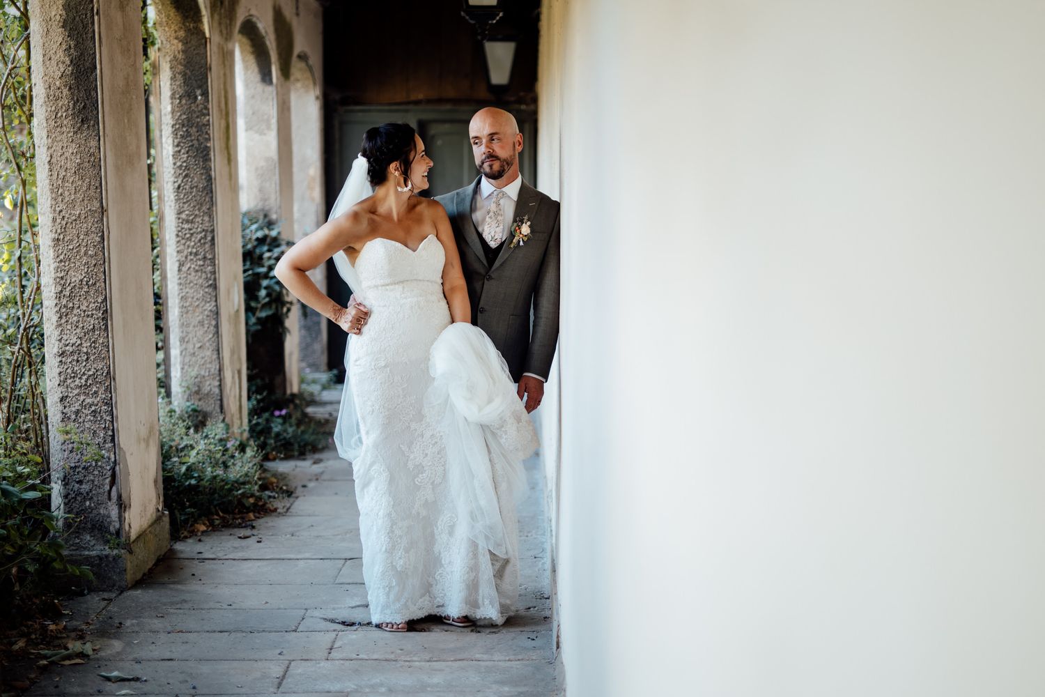 Wedding couple walking through a stone colonnade walkway at a historic venue.
