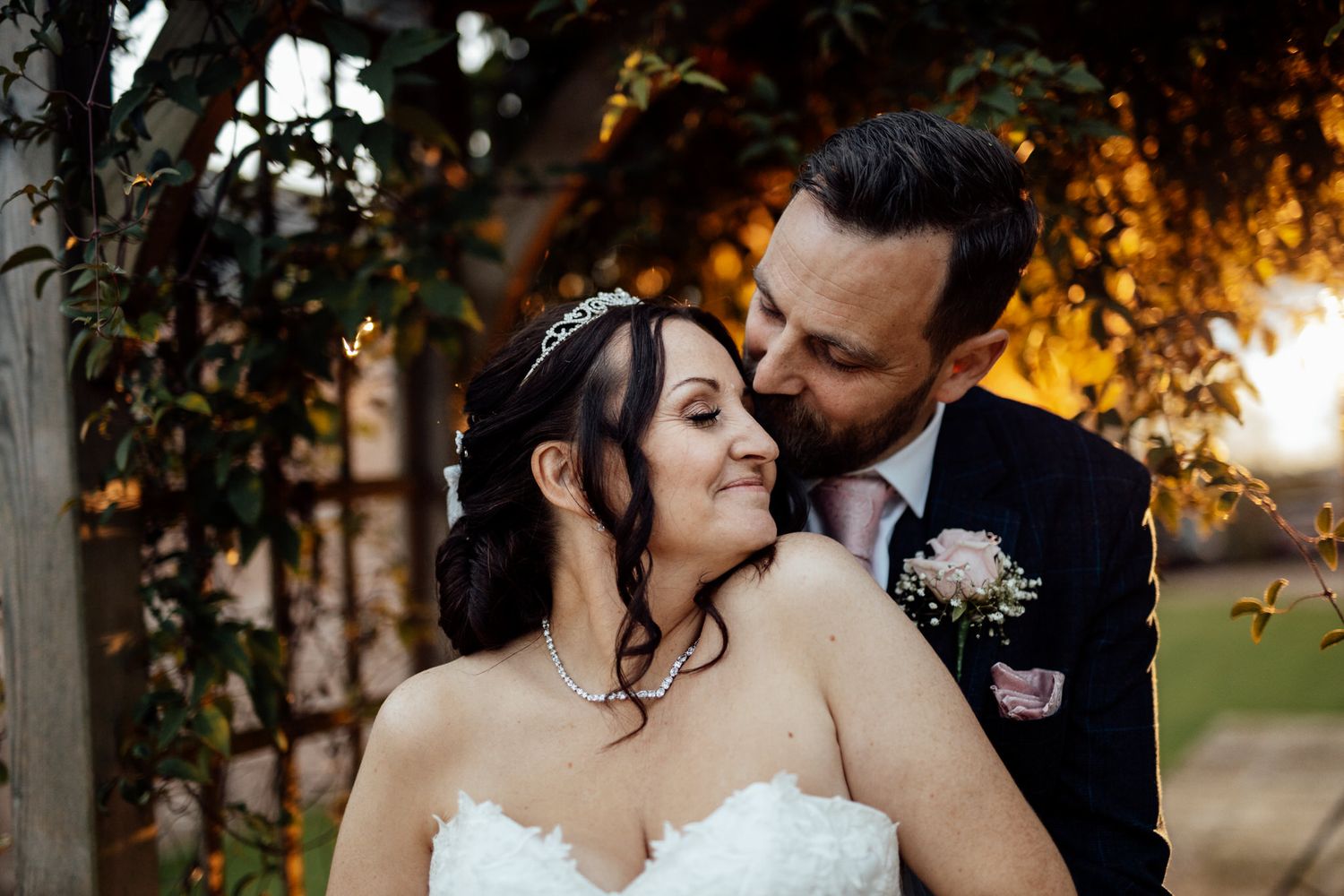 A romantic sunset wedding portrait shows a couple embracing outdoors with warm golden light filtering through trees.