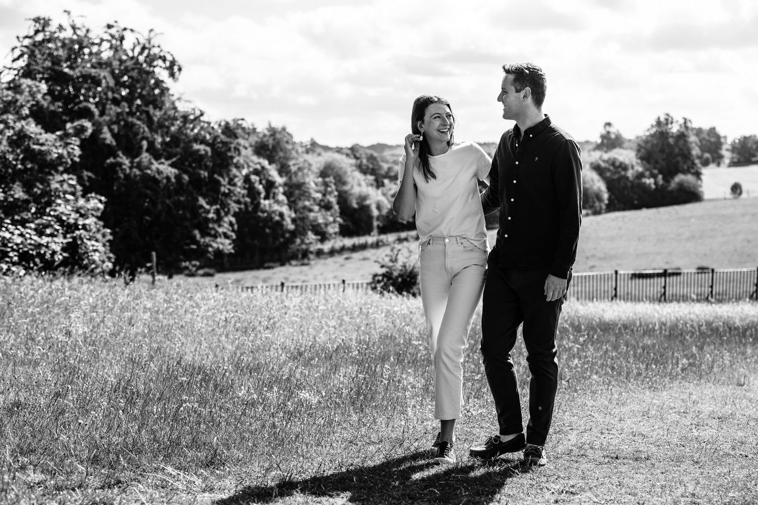 A couple shares a romantic moment in a sunny meadow with trees in the background.