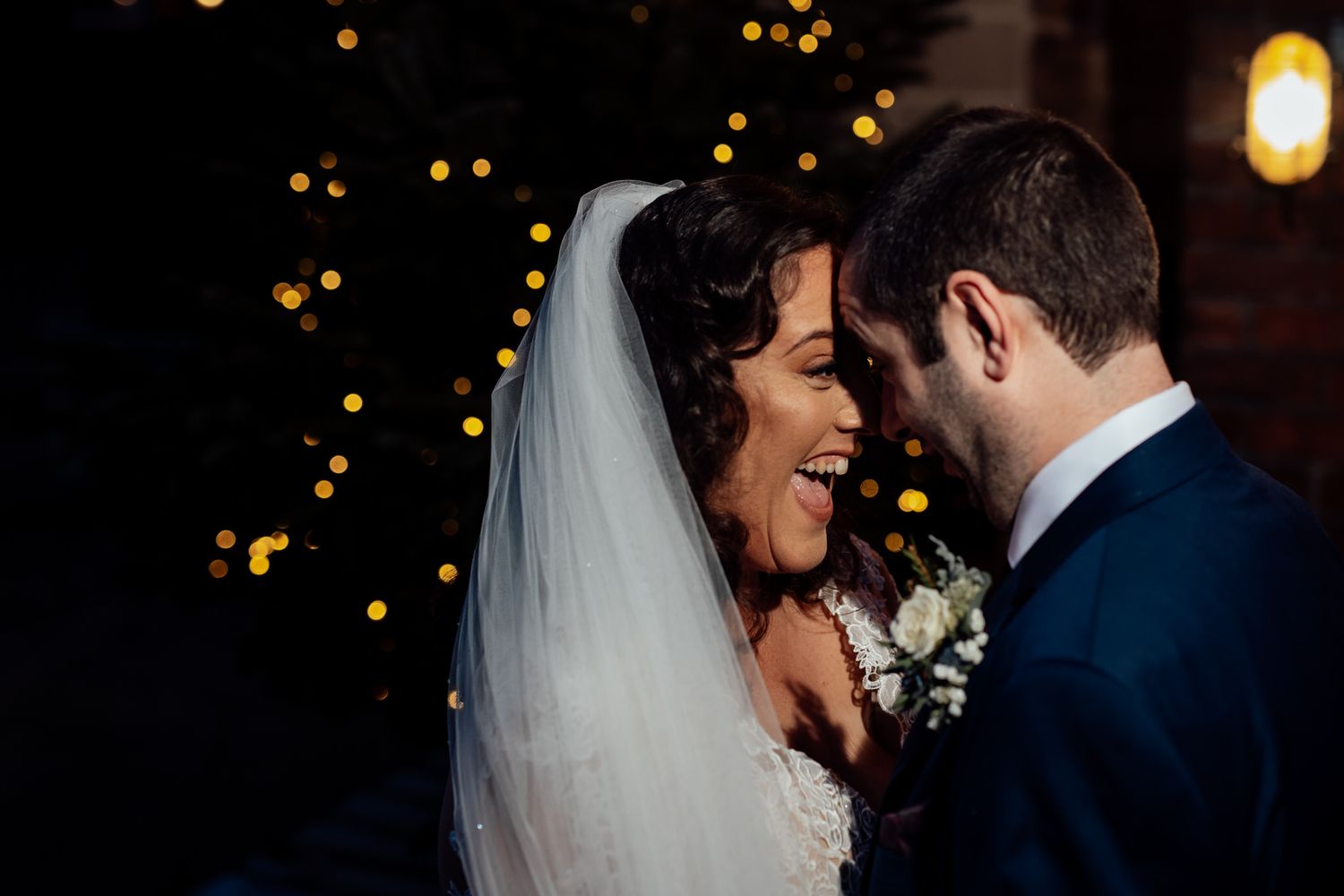 Intimate wedding moment captured in dark setting with bokeh lights.