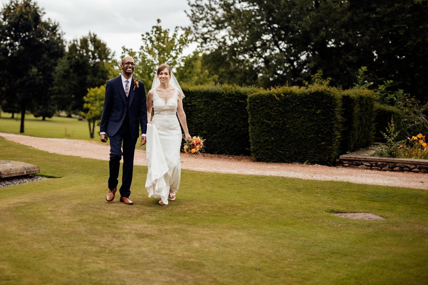Newlyweds walking together on manicured garden grounds.
