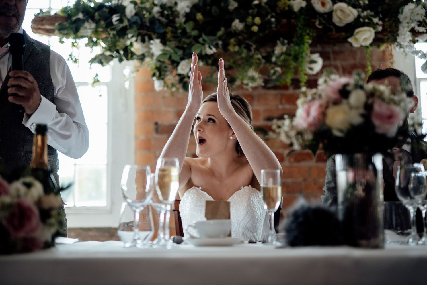 Wedding guest reacts with excitement at reception table decorated with floral centerpieces.