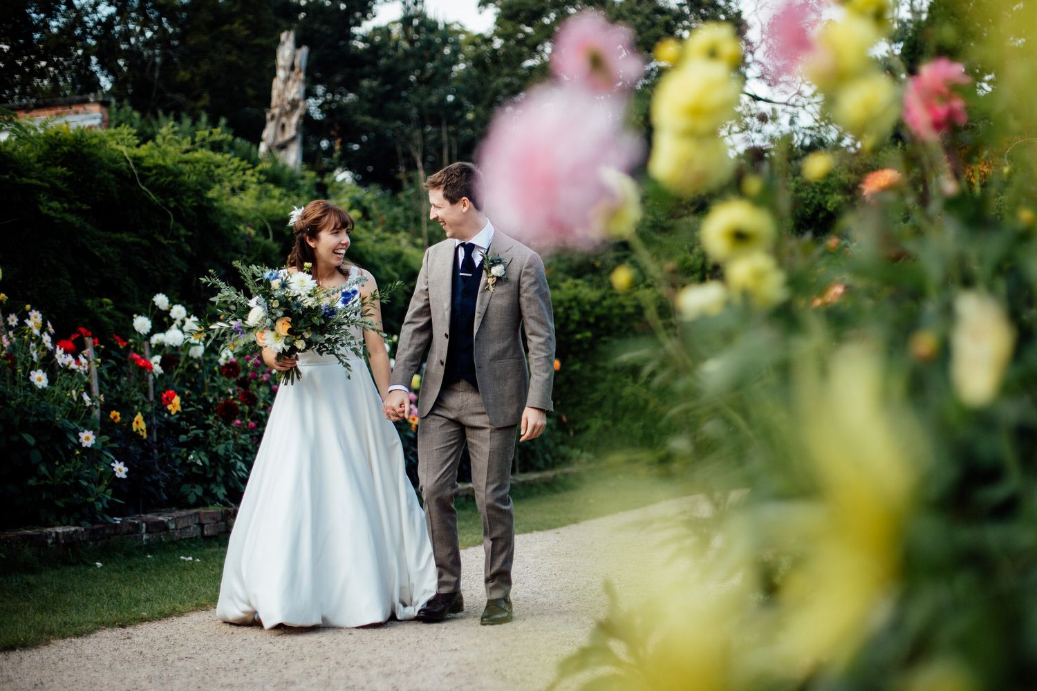 Couple walking through garden path with colorful flowers in foreground.
