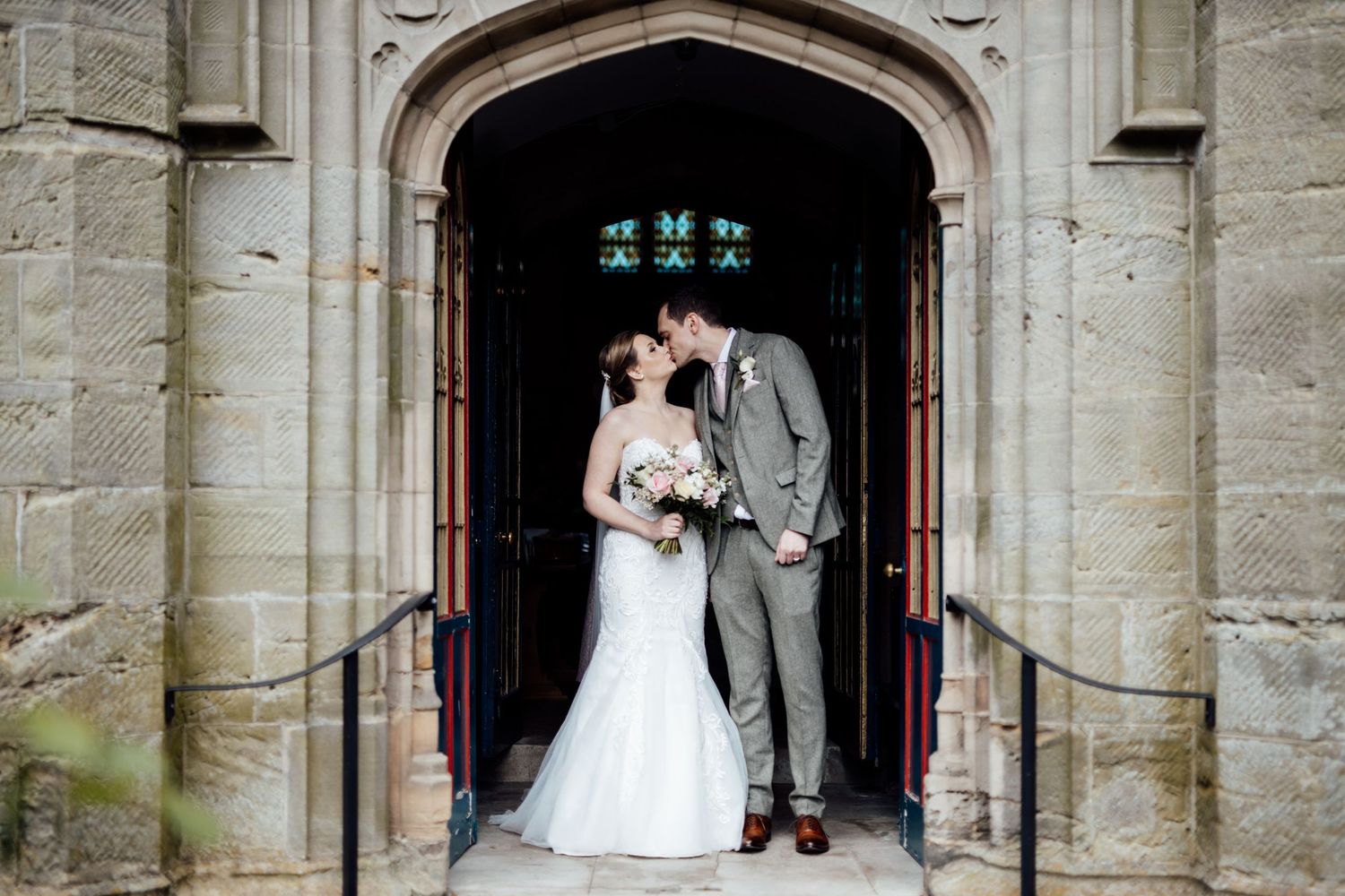 Wedding ceremony takes place under grand stone archway of historic church.