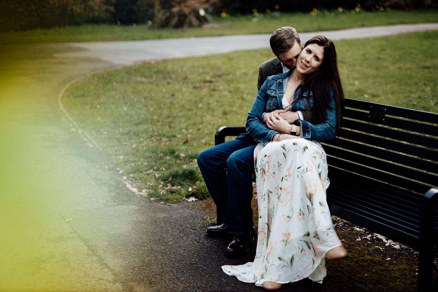 A couple shares romantic moments on a park bench surrounded by greenery.