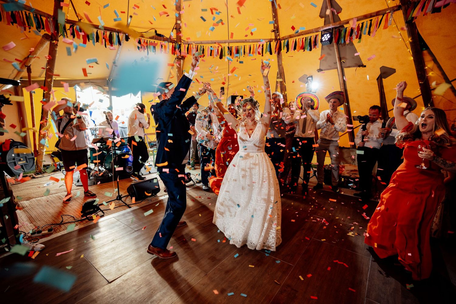 Wedding reception celebration under an orange-lit tent with confetti and festive decorations.