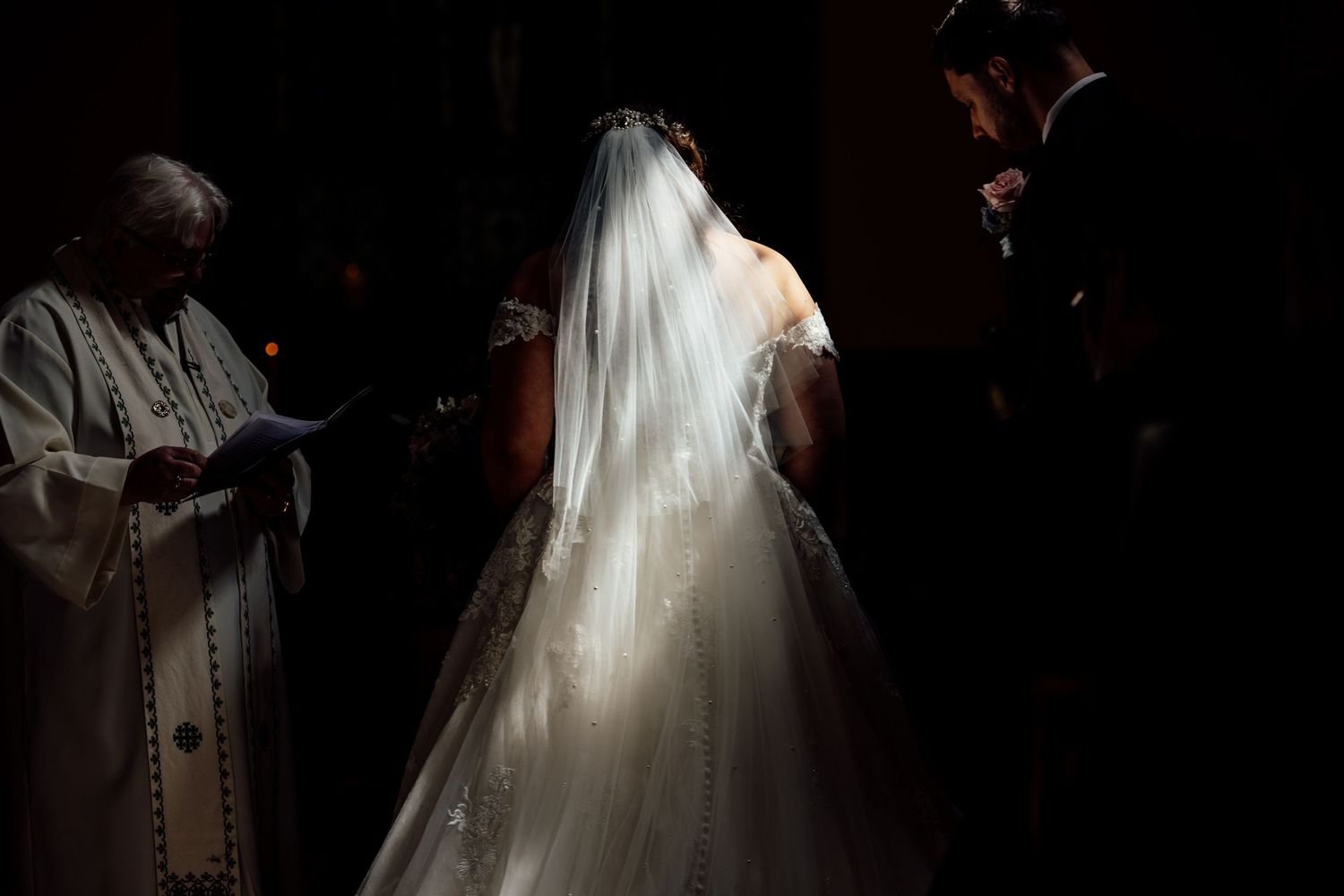 Dramatic silhouettes of wedding ceremony participants in dark venue.