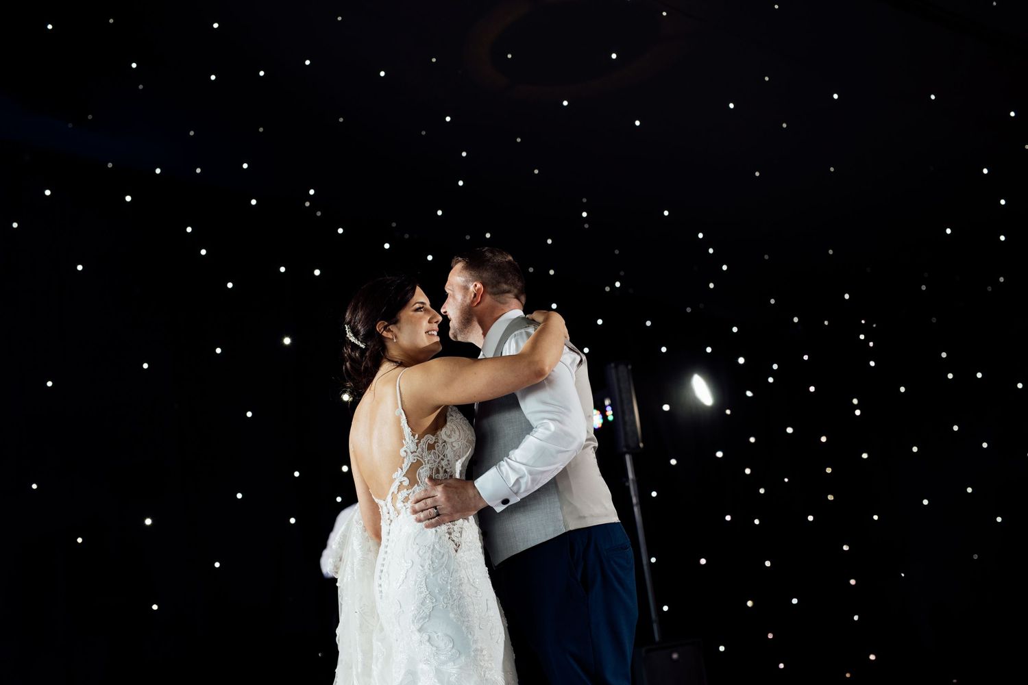 Couple dancing under twinkling lights at evening reception.