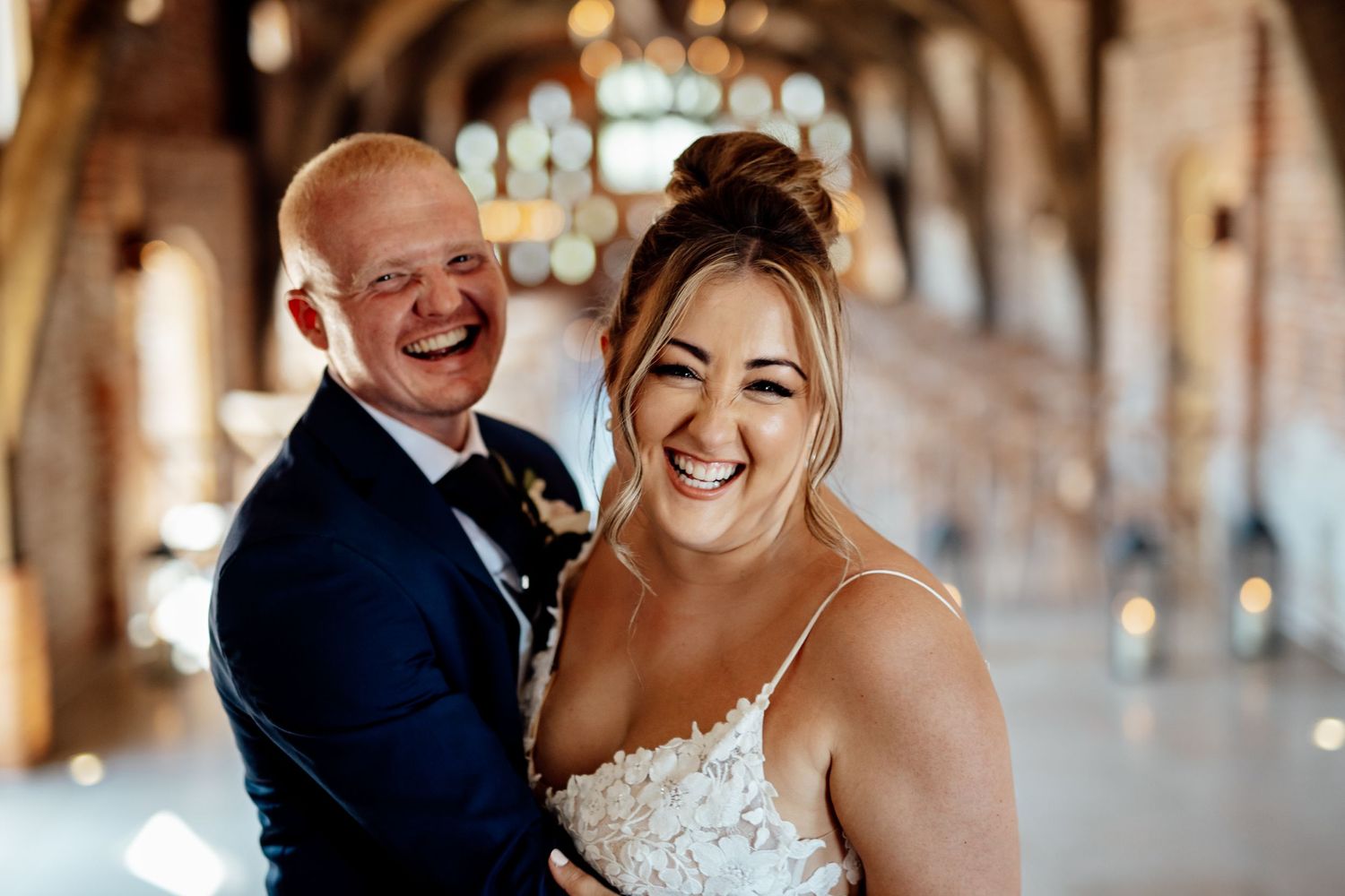 Candid moments of laughter and joy captured in rustic brick venue during wedding celebration.