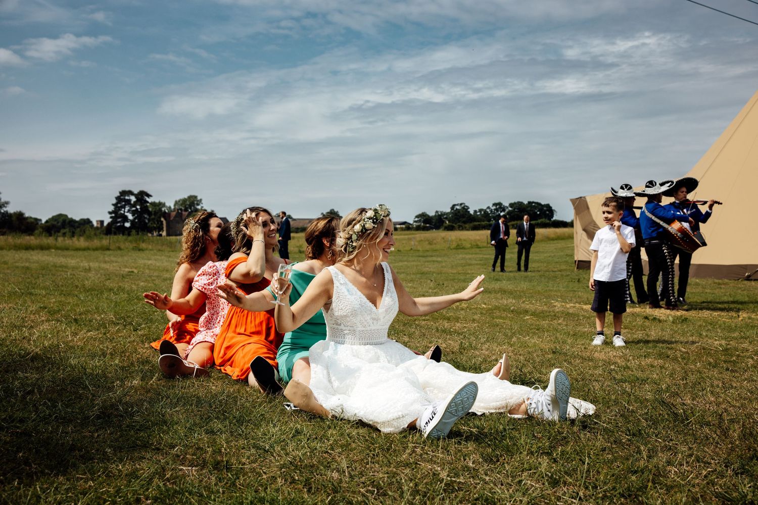 Wedding party poses for creative group photo on grassy field near tent.
