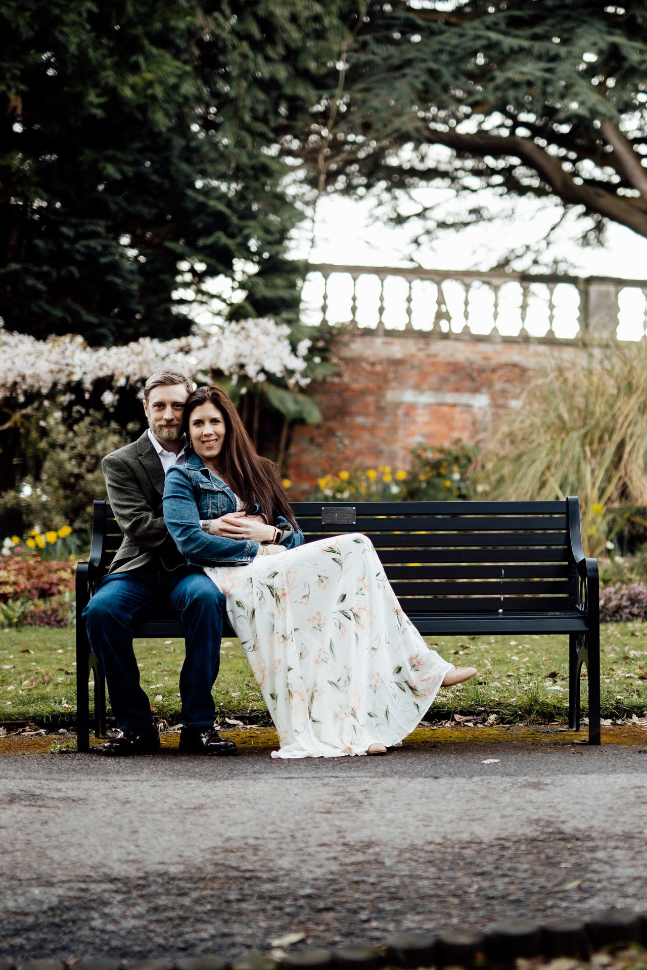 A couple shares an intimate moment while sitting together on a wooden bench in a garden setting.