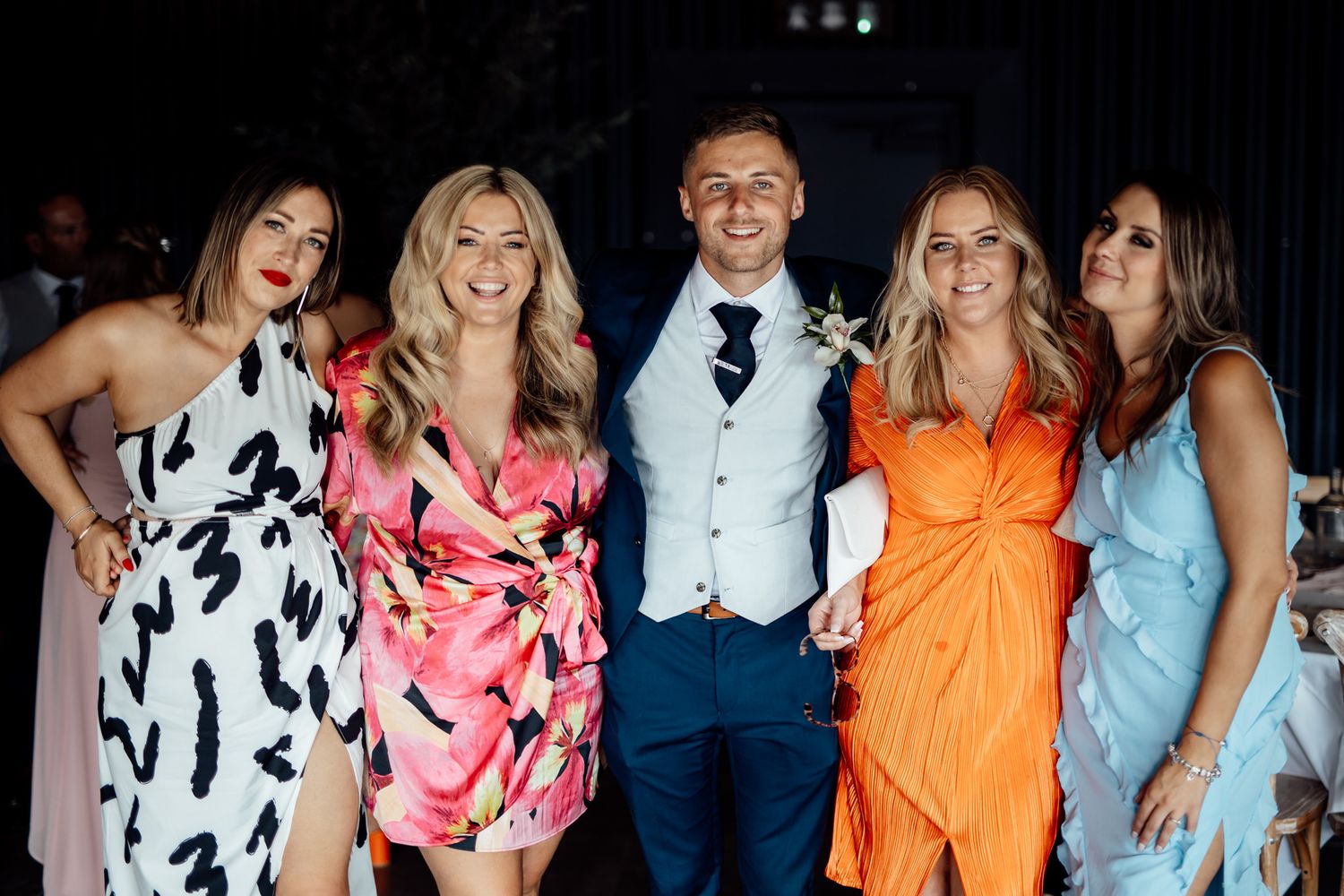 Wedding party in colorful dresses including orange, pink and blue poses together.