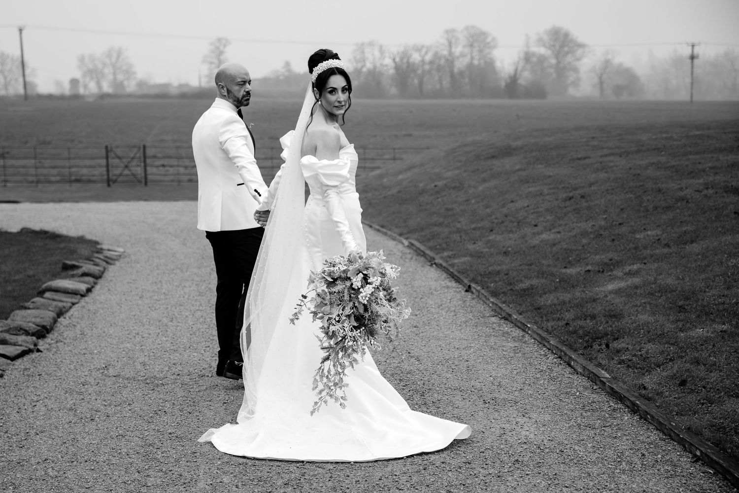 Black and white wedding portraits captured on misty countryside path.