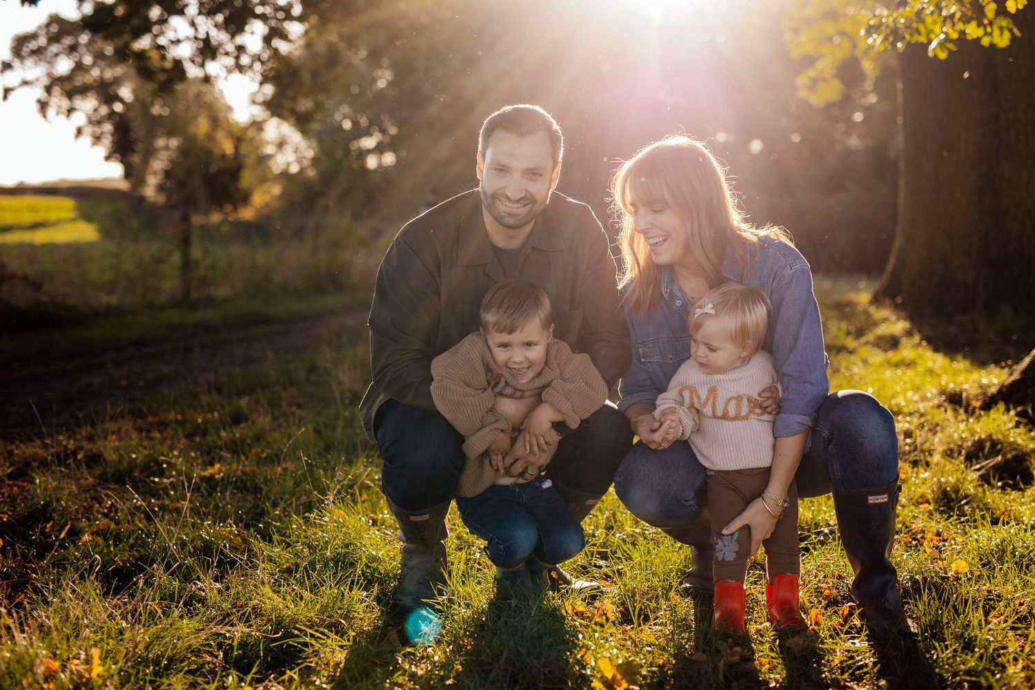 Family laughing together in sunlit autumn field with golden bokeh.