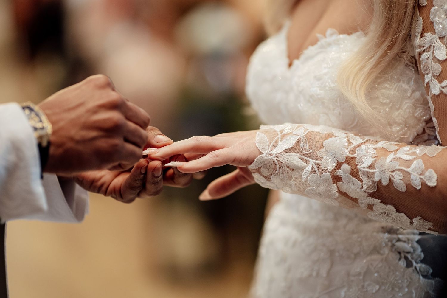 Groom places a wedding ring on brides finger during ceremony in lace long sleeve gown.
