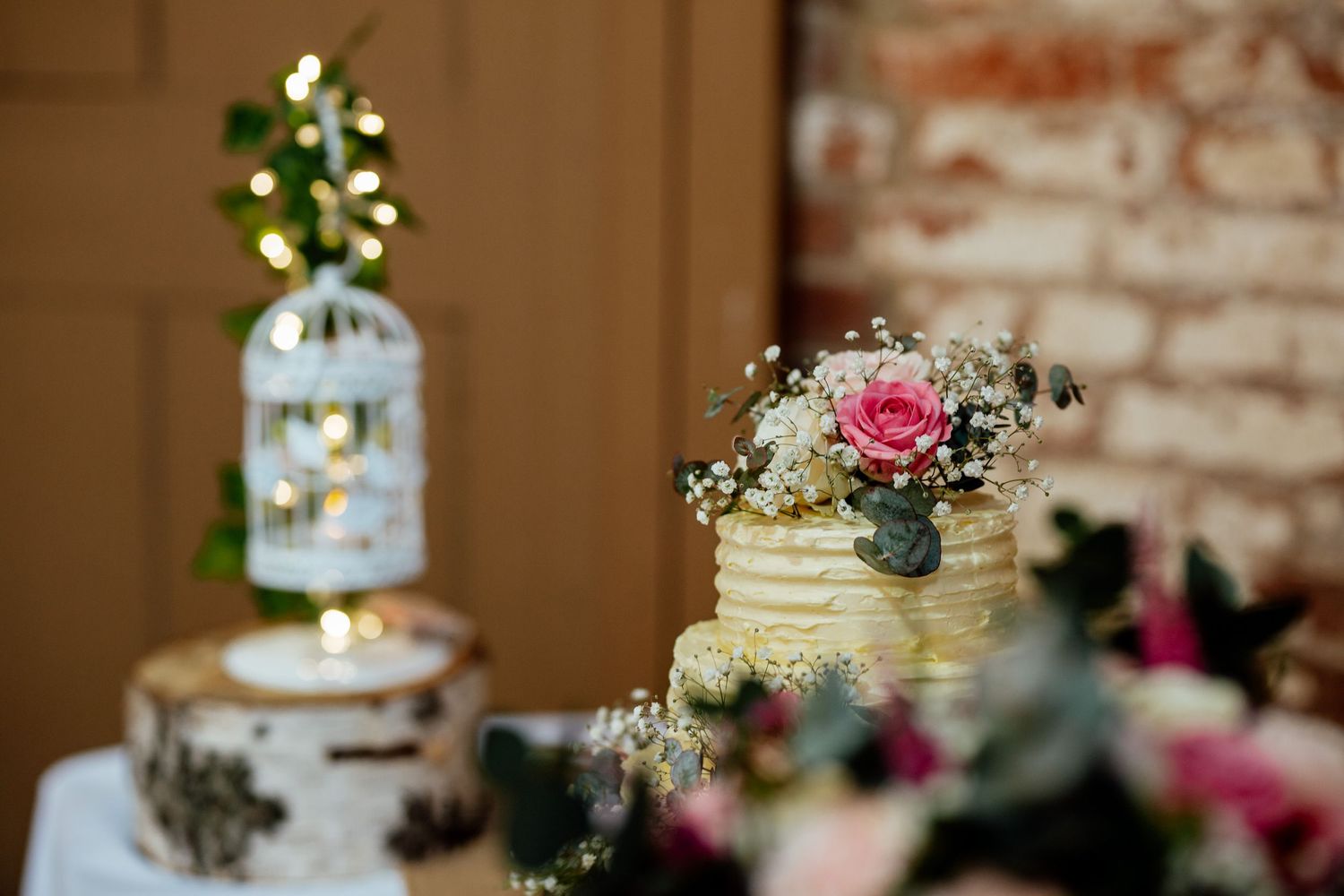 Elegant wedding cake display with multiple tiers adorned with fresh flowers and rustic decor against exposed brick wall.