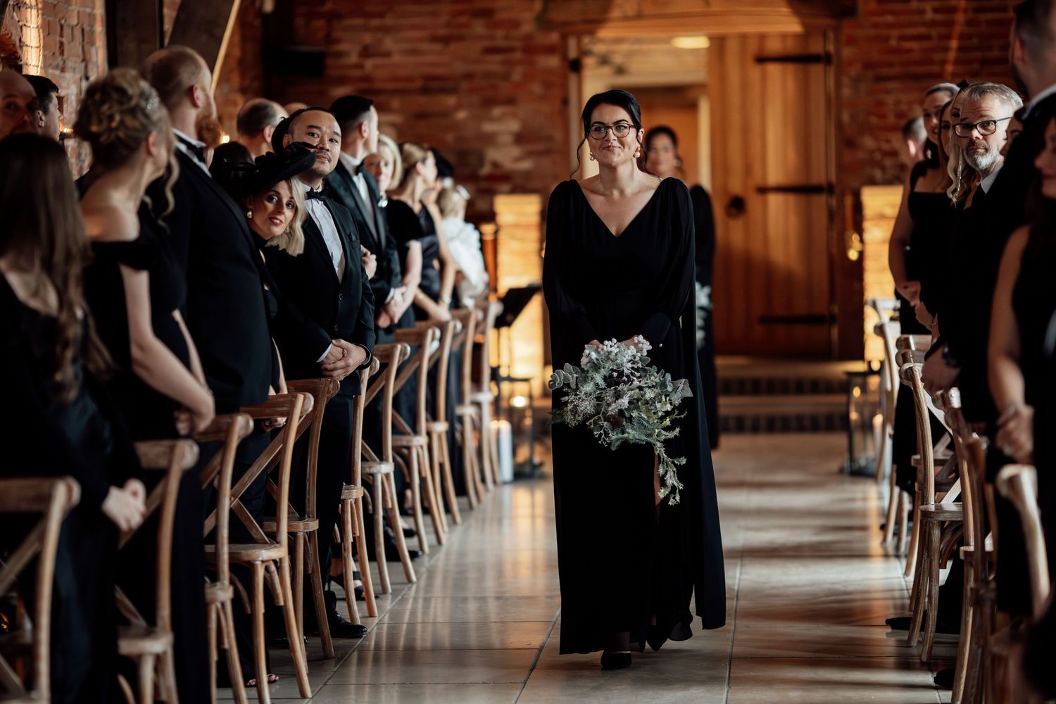 Guests seated in wooden chairs inside a rustic brick venue during a ceremony.
