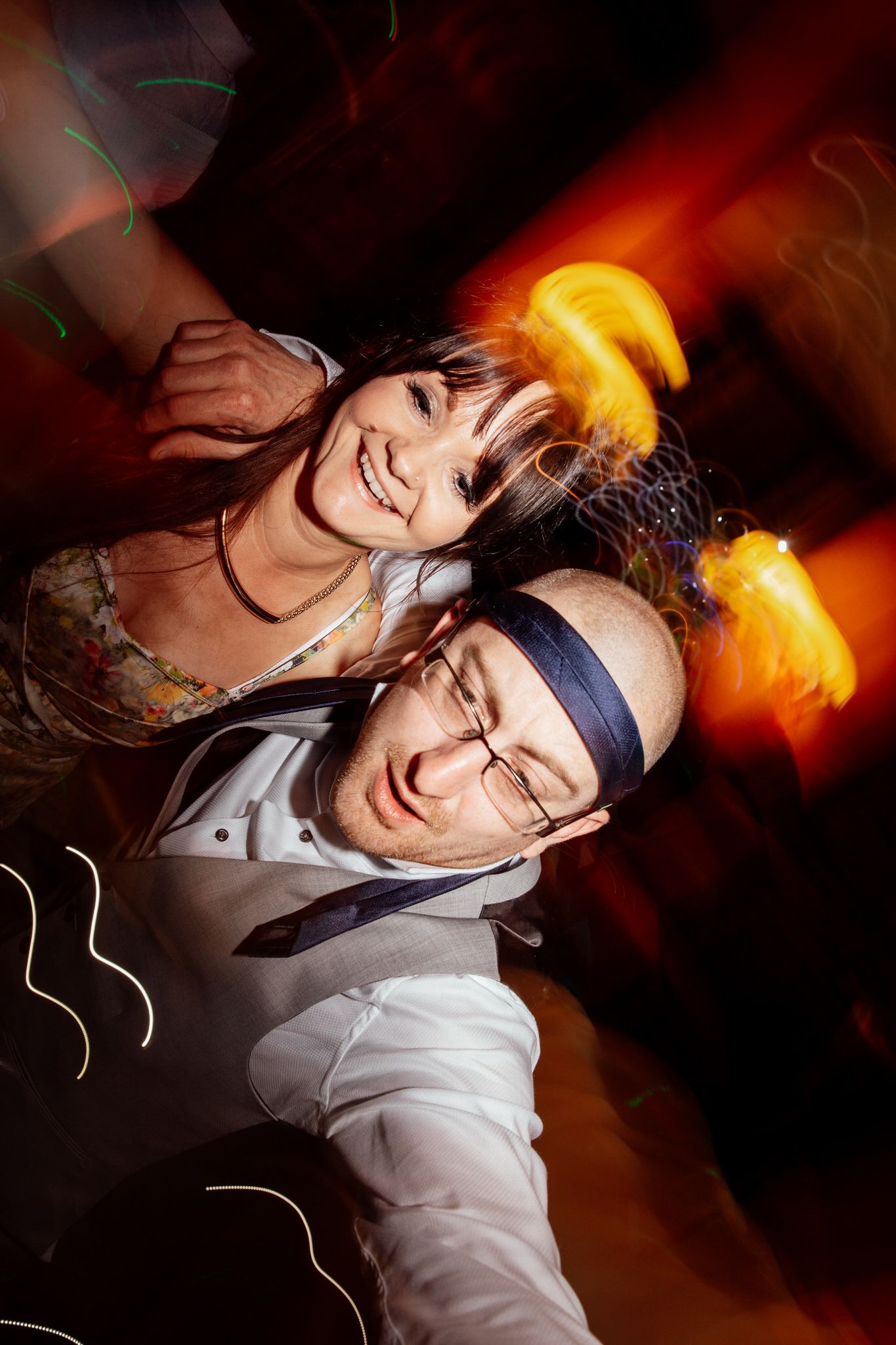 Dance floor celebration with dramatic orange lighting at evening wedding reception.