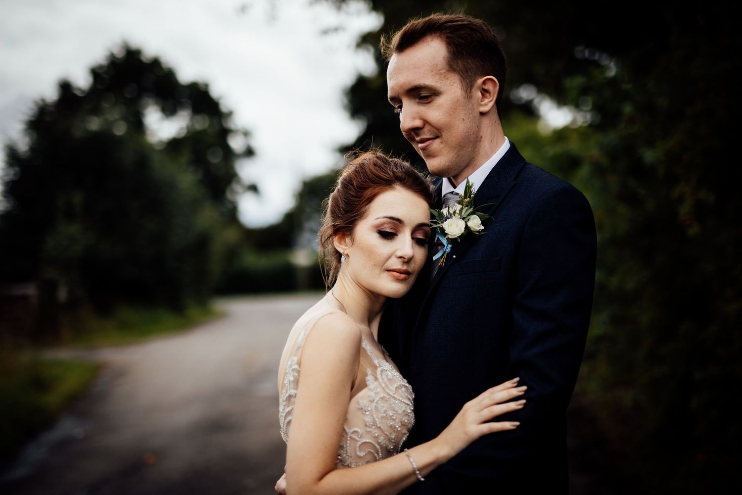 Romantic wedding portrait with couple embracing against a dark natural backdrop.