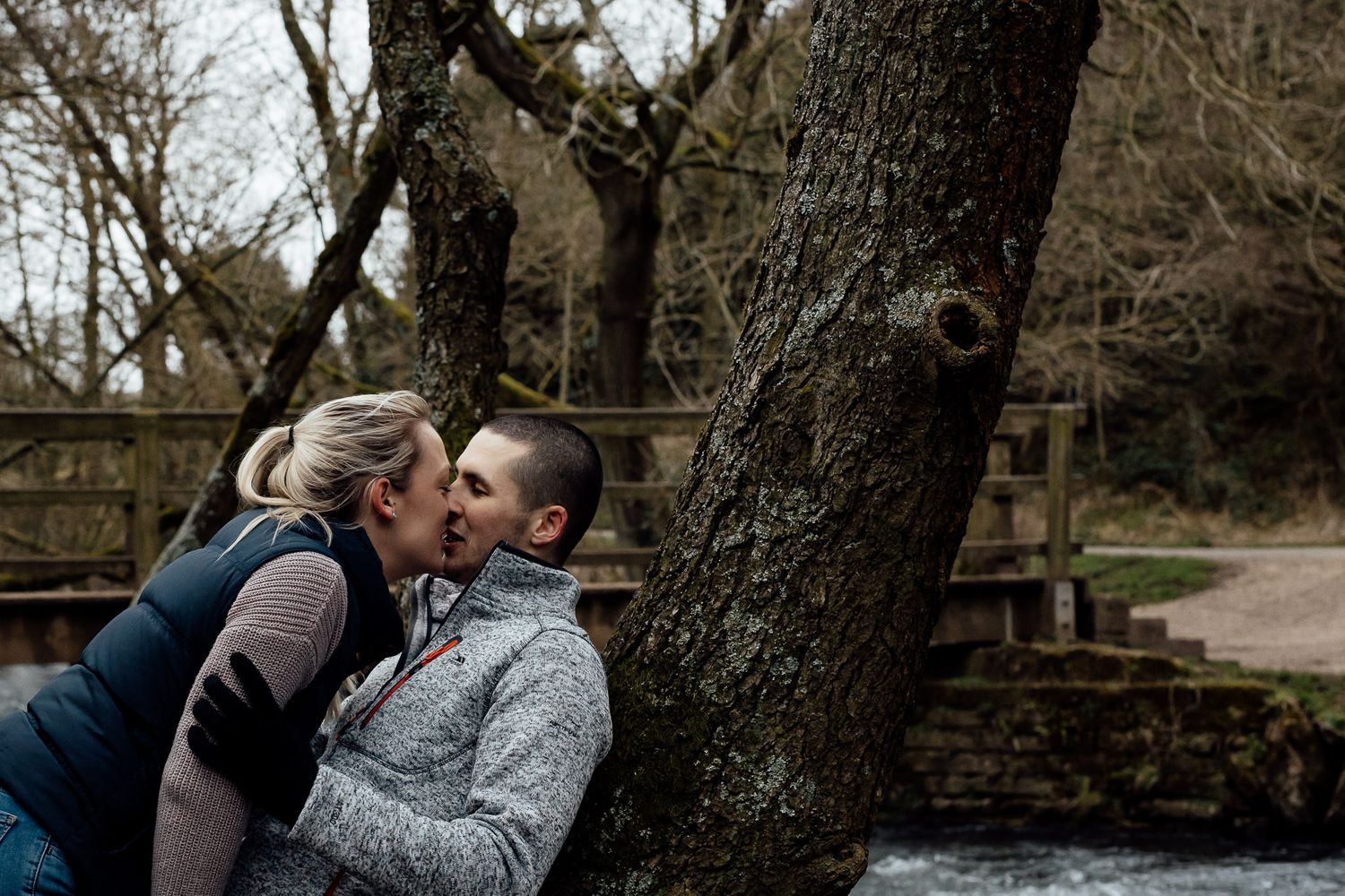Two people sharing an intimate moment beside a large tree trunk.