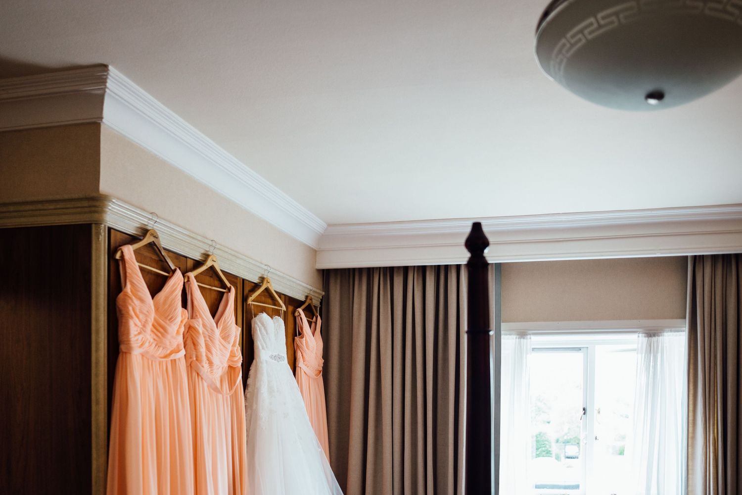 Peach colored bridesmaid dresses hanging in a hotel room window with natural light.