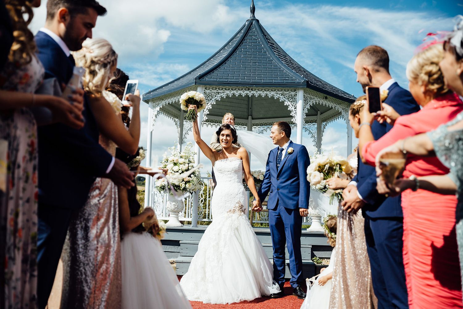 Wedding ceremony and celebration at outdoor gazebo venue under bright blue skies.