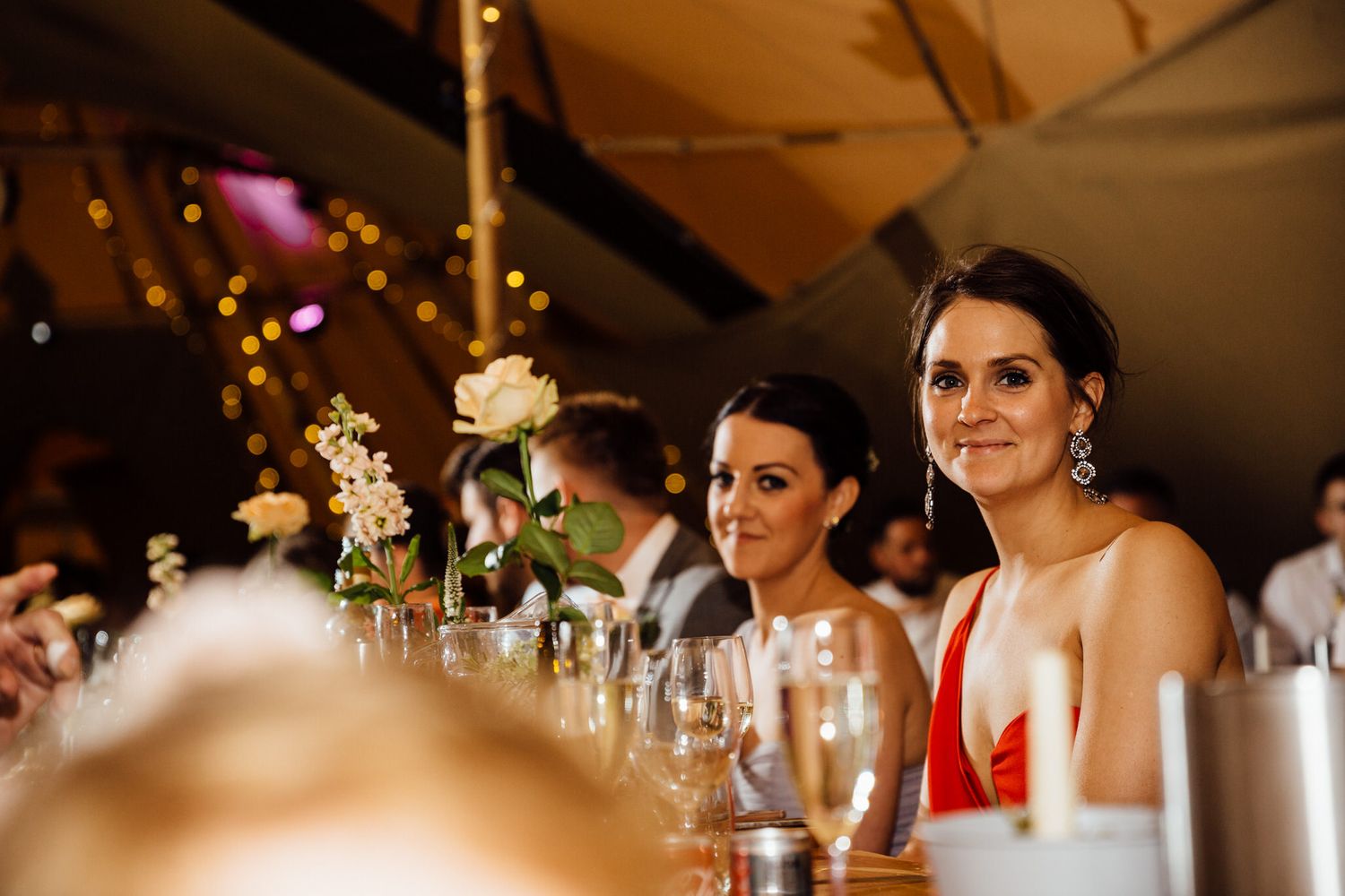 Elegant table settings and decorations at a tipi wedding reception with string lights overhead.