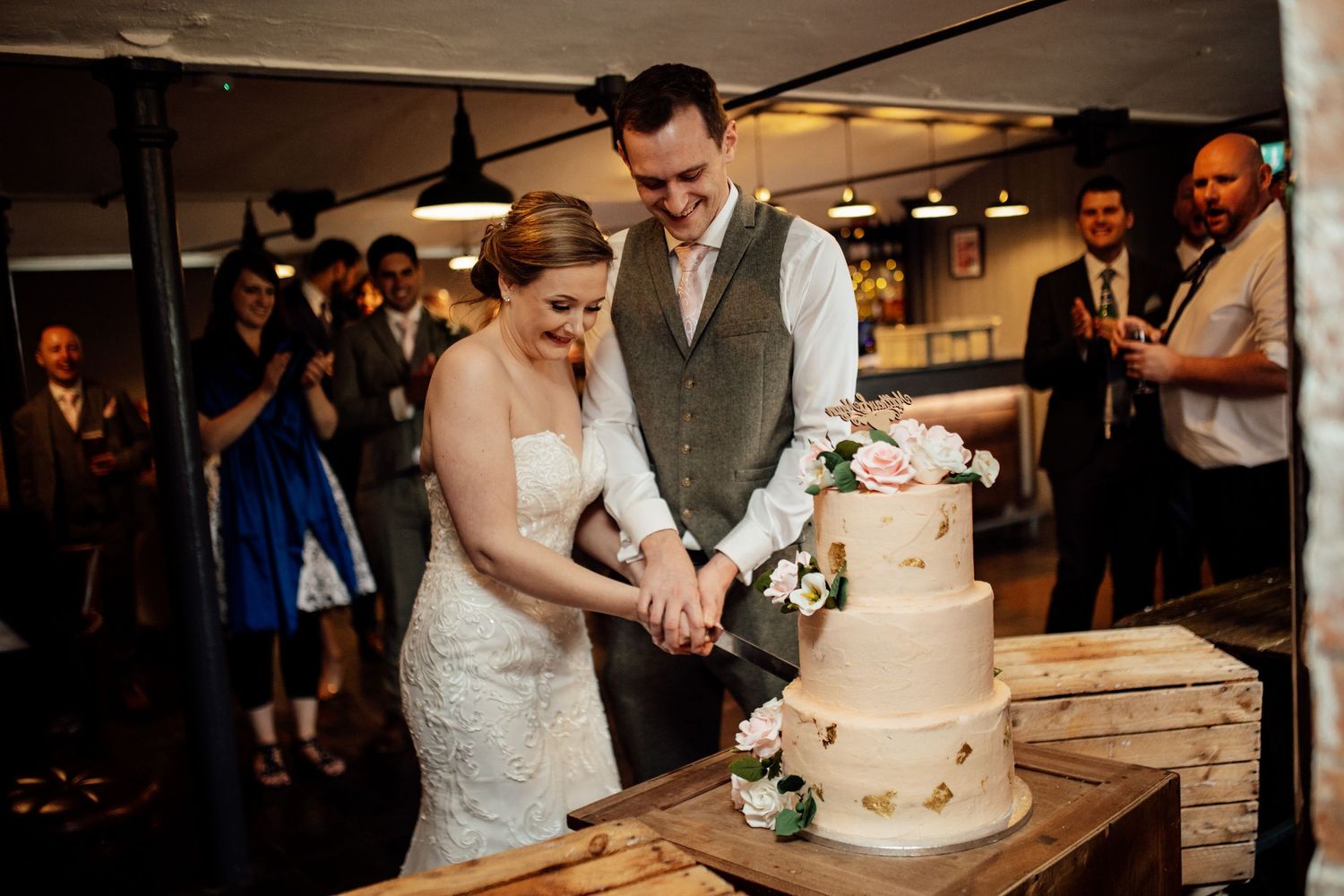 Wedding cake cutting ceremony with guests watching in a rustic indoor venue.