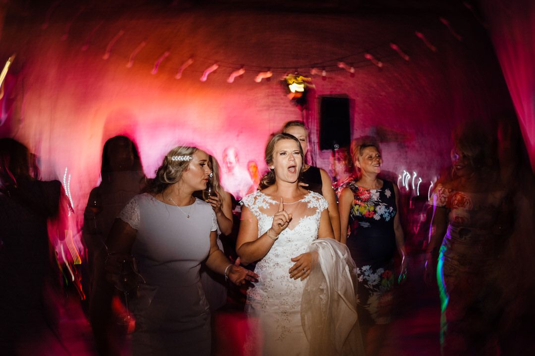 Dance floor filled with wedding guests under dramatic pink lighting.
