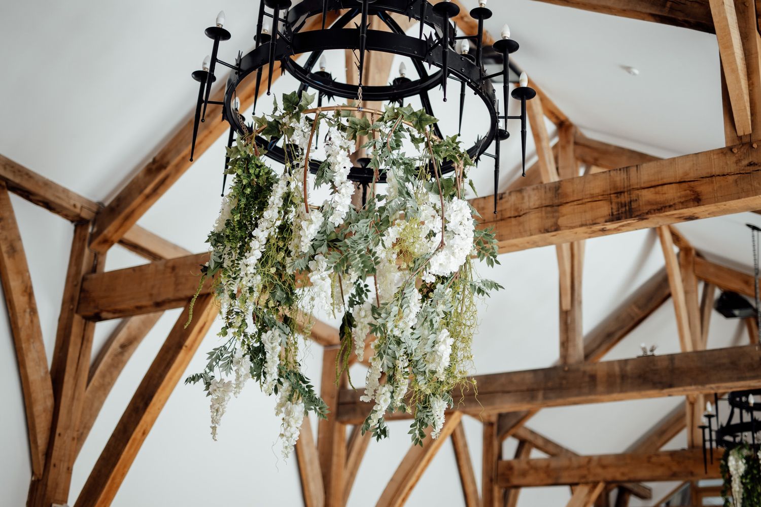 Rustic wooden beams and hanging floral arrangements decorate an elegant wedding venue ceiling.