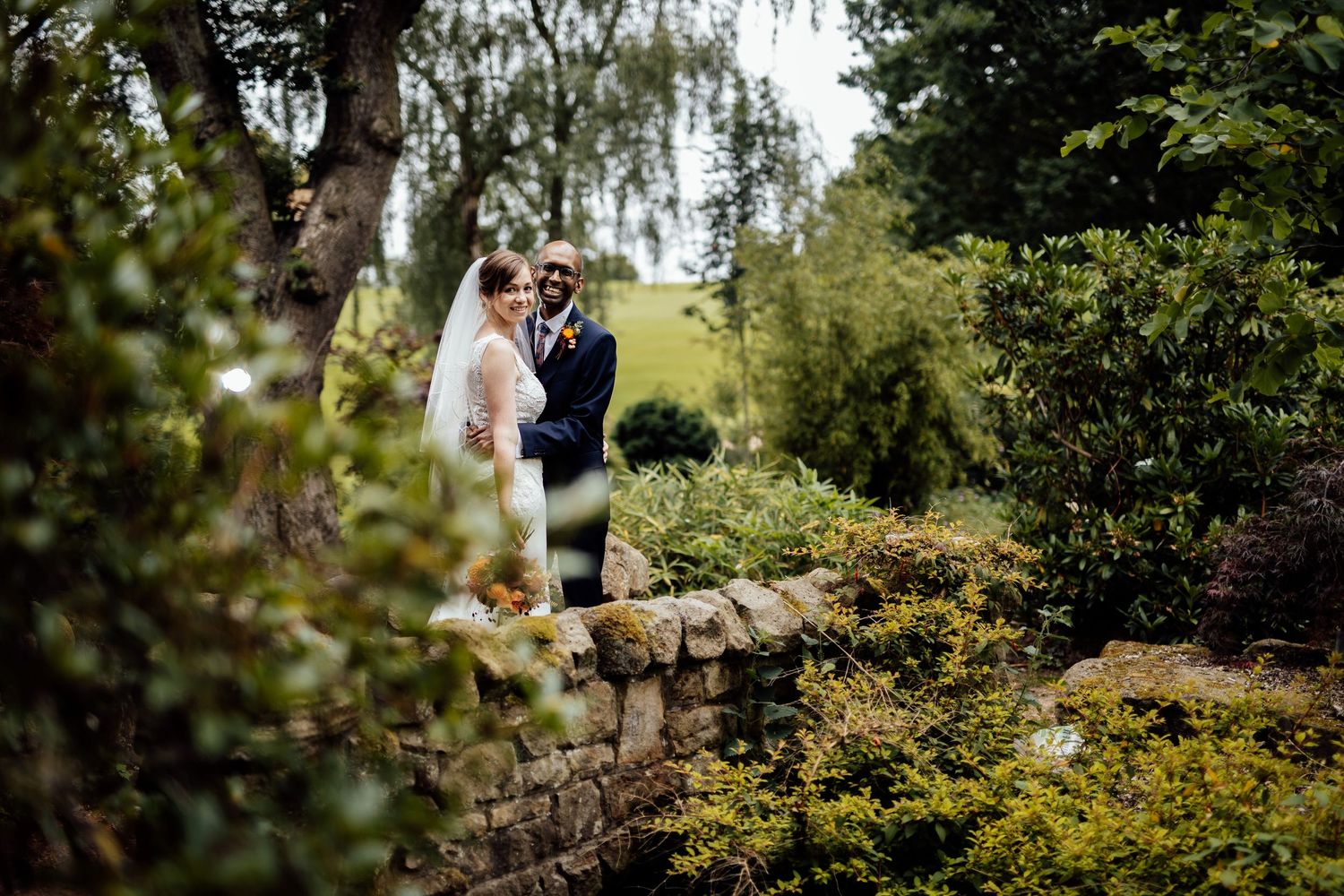 Wedding couple poses in lush garden setting with beautiful greenery and natural lighting.