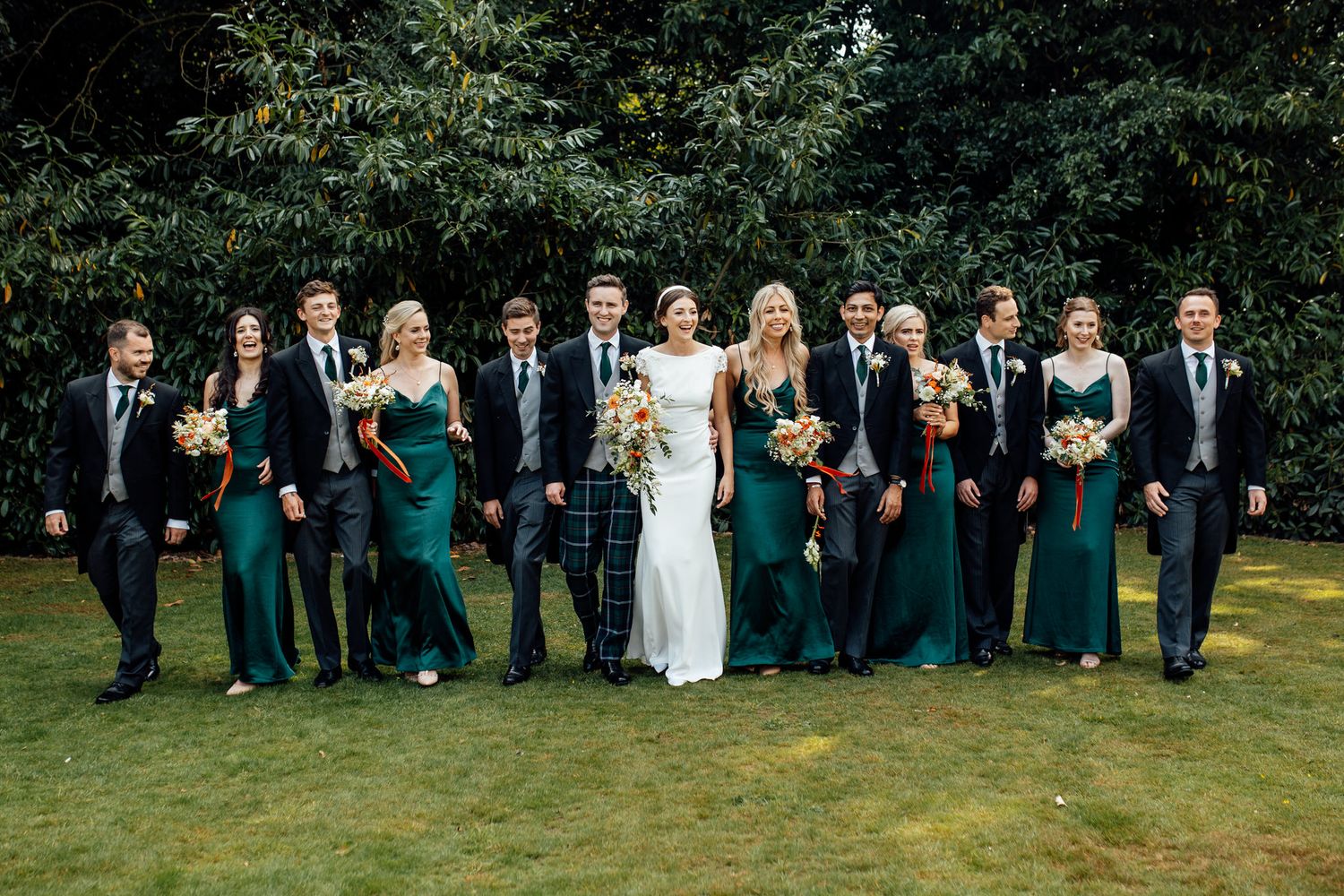 Large wedding party lined up for formal photo in green and black attire.