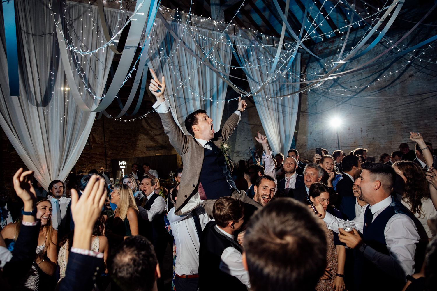 Wedding reception dance party with dramatic blue lighting and guests dancing in a decorated venue.