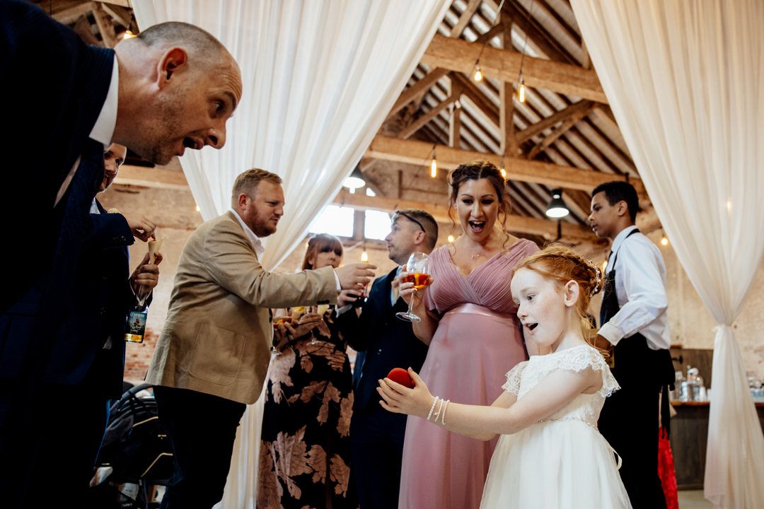 Wedding guests mingling and dancing at an indoor reception with white decor.