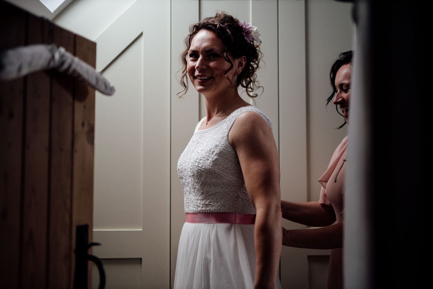 Elegant wedding dress detail with lace bodice and pink sash in natural lighting.