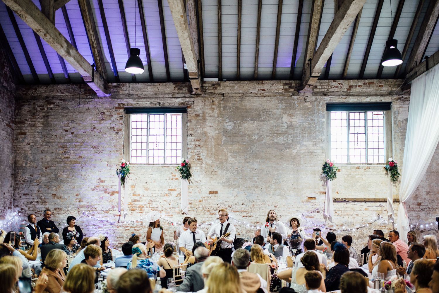 Panoramic view of a wedding reception in a converted industrial space with dramatic lighting.