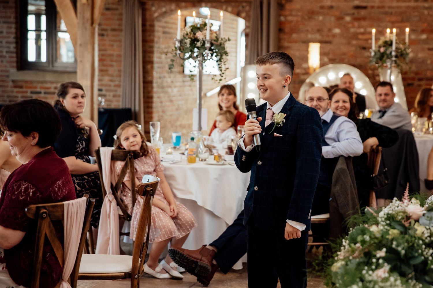 Wedding reception in rustic brick venue with guests gathered around decorated tables.
