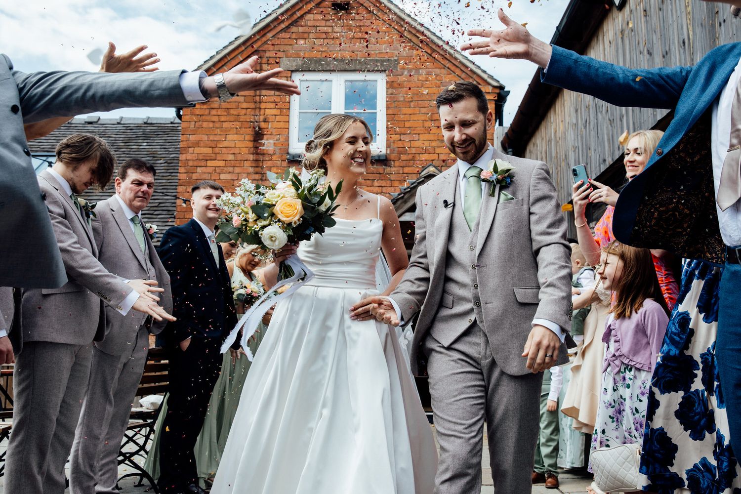 Wedding party posing for group photos outside a rustic brick building.