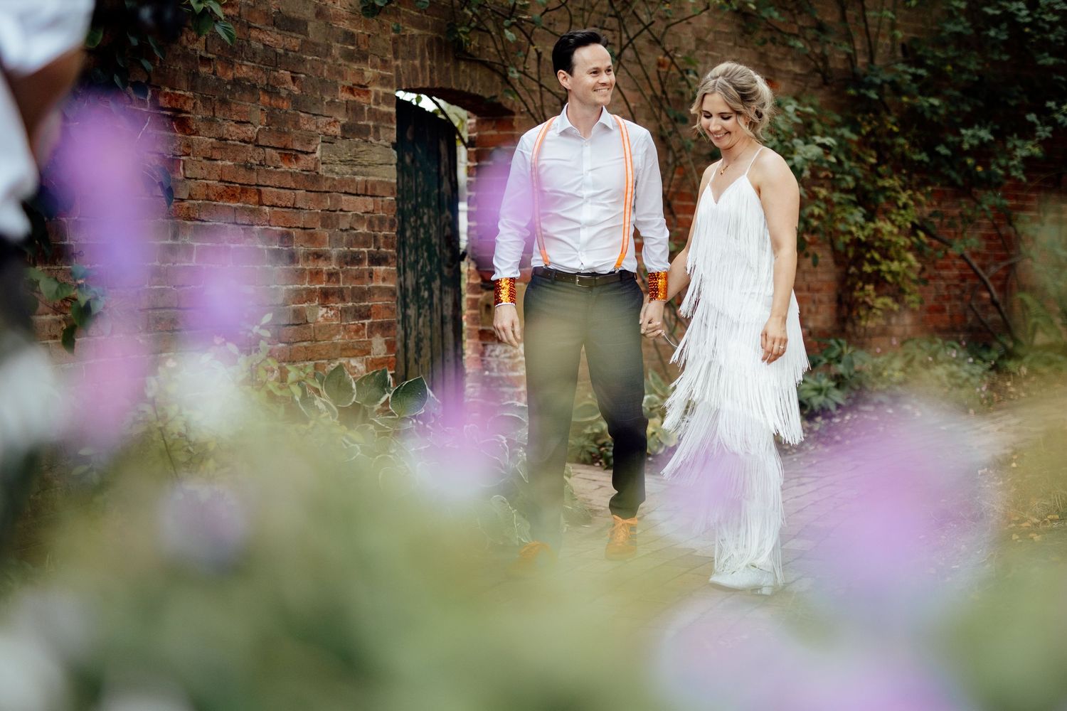 Garden wedding ceremony with purple flowers and brick wall backdrop.
