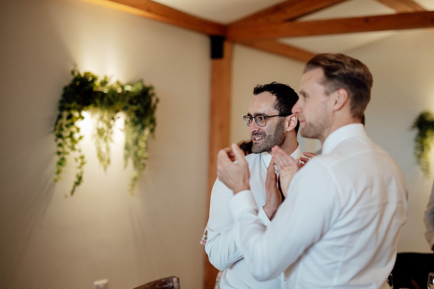 Two guests share a moment during wedding reception under decorative greenery.