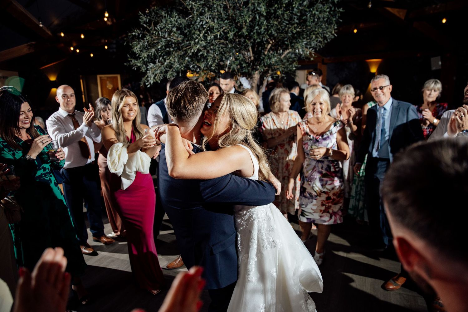 Wedding party dances and celebrates on dimly lit dance floor at reception.