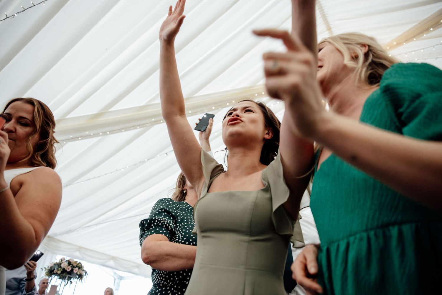 Joyful wedding guests dancing and celebrating under white tent reception.