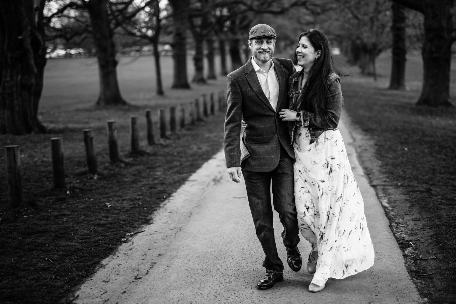 Couple walking together through park pathway during autumn photoshoot.