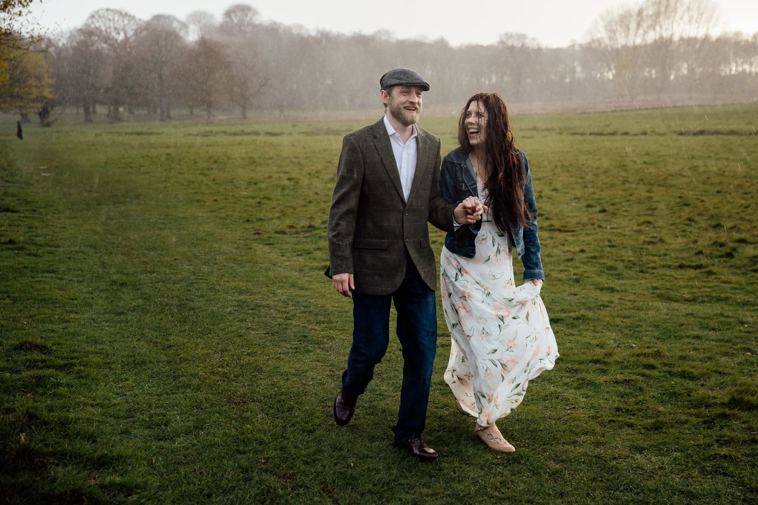 A couple strolls across a grassy field on an overcast day.