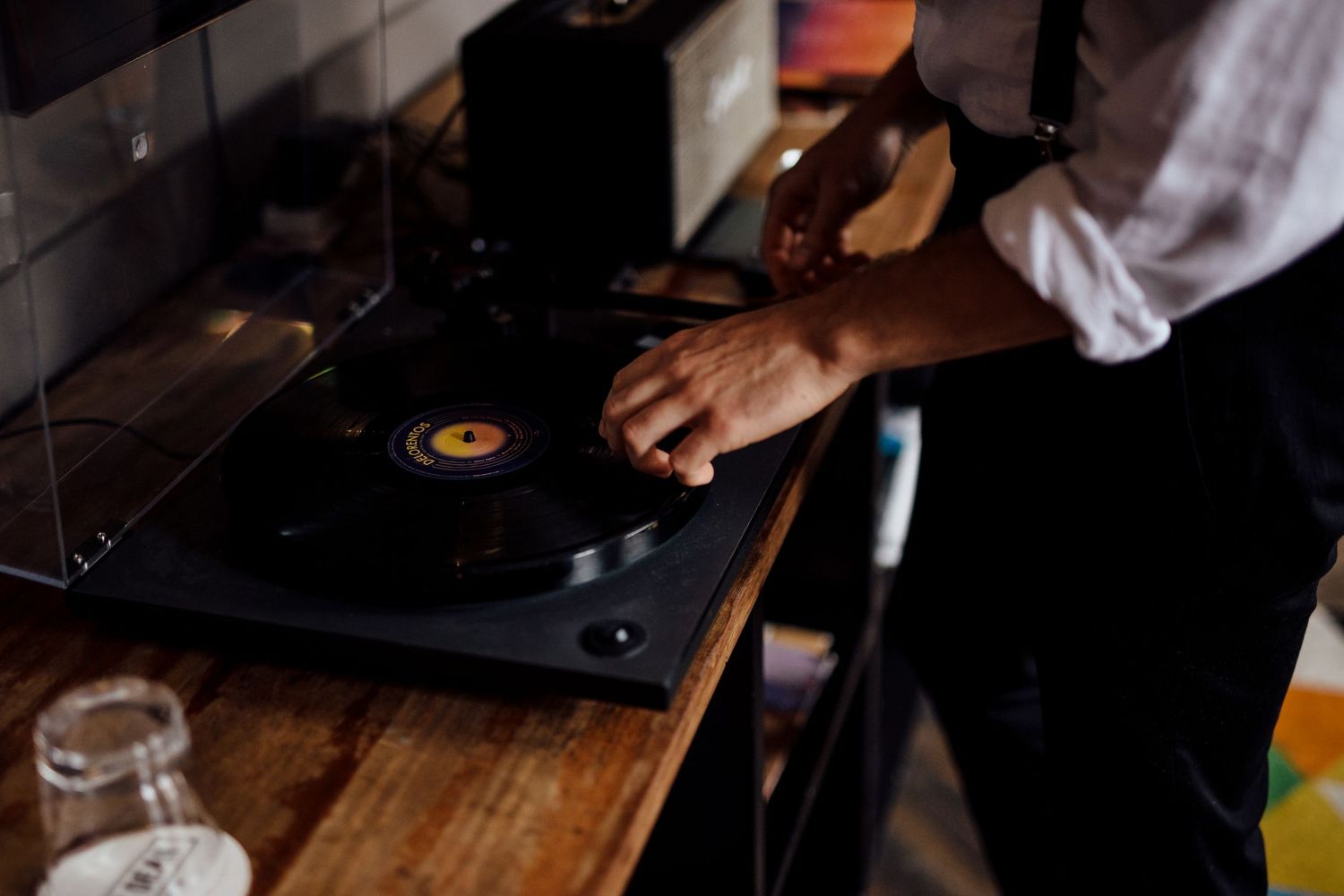 Close-up of hands operating vinyl turntable on wooden surface.