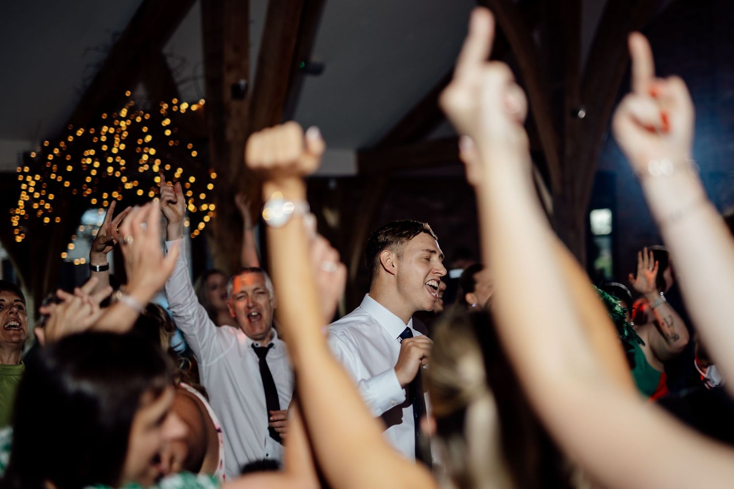 Silhouettes of wedding guests dancing and raising hands during an energetic reception celebration.