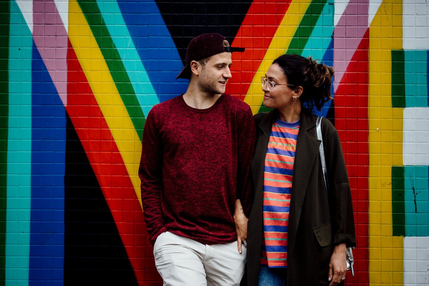 Couple standing against vibrant rainbow striped wall mural in urban setting.